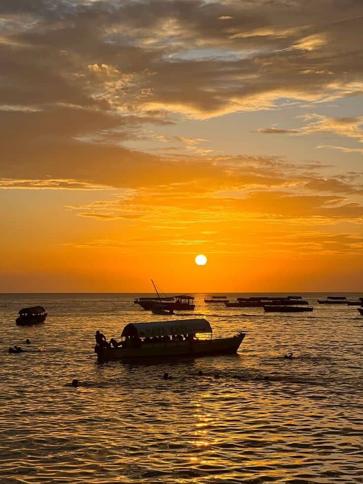 Traditional dhow boats silhouetted against a glowing orange Zanzibar sunset